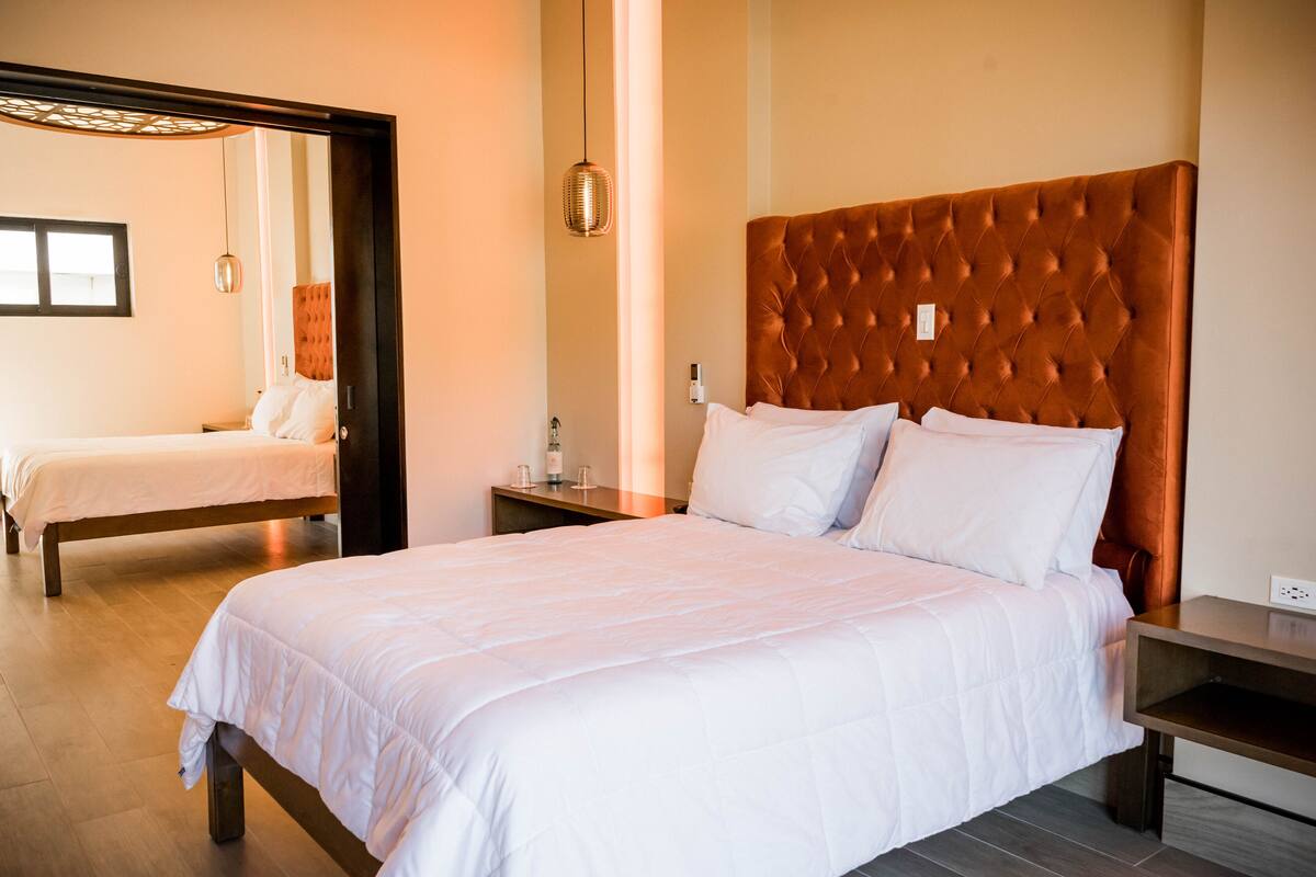 Une chambre d’hôtel avec deux lits, une tête de lit en bois, une table de chevet et un miroir.