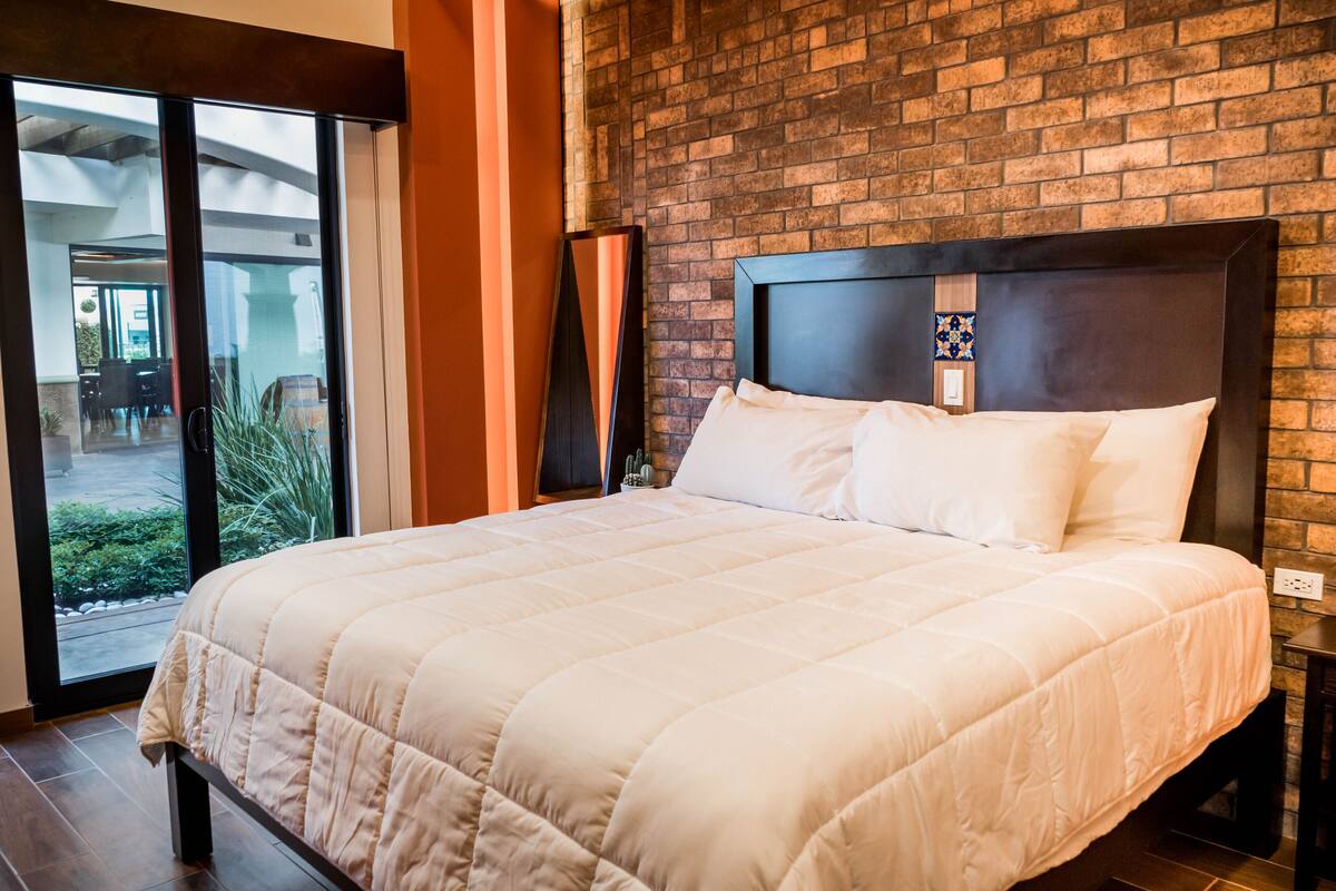 Un grand lit avec une couette blanche matelassée, une tête de lit sombre et un mur en briques derrière.
