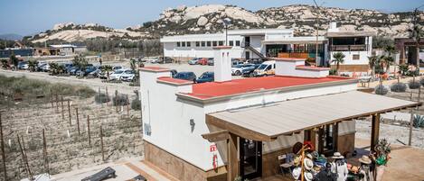 A hotel with a red roof, a covered outdoor area with a wooden bench, and a mountain backdrop.