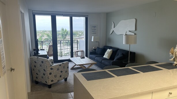 Un salon moderne avec un canapé, un fauteuil à motifs, une table basse et une vue sur la ville grâce à de grandes fenêtres.