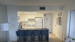 Une cuisine compacte dotée d’un îlot central, de quatre tabourets de bar, d’un réfrigérateur et d’une cuisinière.
