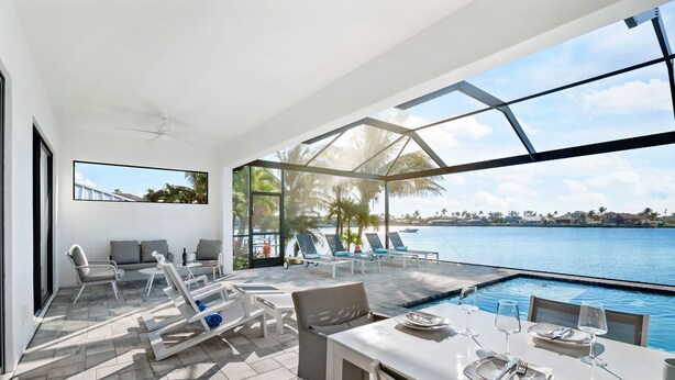 A modern outdoor dining area with a pool, sun loungers, and a view of the water.