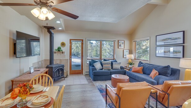 A spacious living area with a fireplace, a blue sofa, orange chairs, and a dining table set for four. - Cloudcroft Vacation Rental ~ 4 Mi to Skiing! (Cloudcroft)
