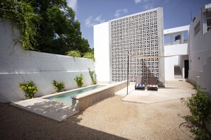 Un espacio exterior moderno con piscina, mobiliario y una pared blanca con diseño de celosía.
