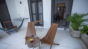En terrasse med to træstole, et rundt bord med en skål og to vinglas, samt en hængekøje.