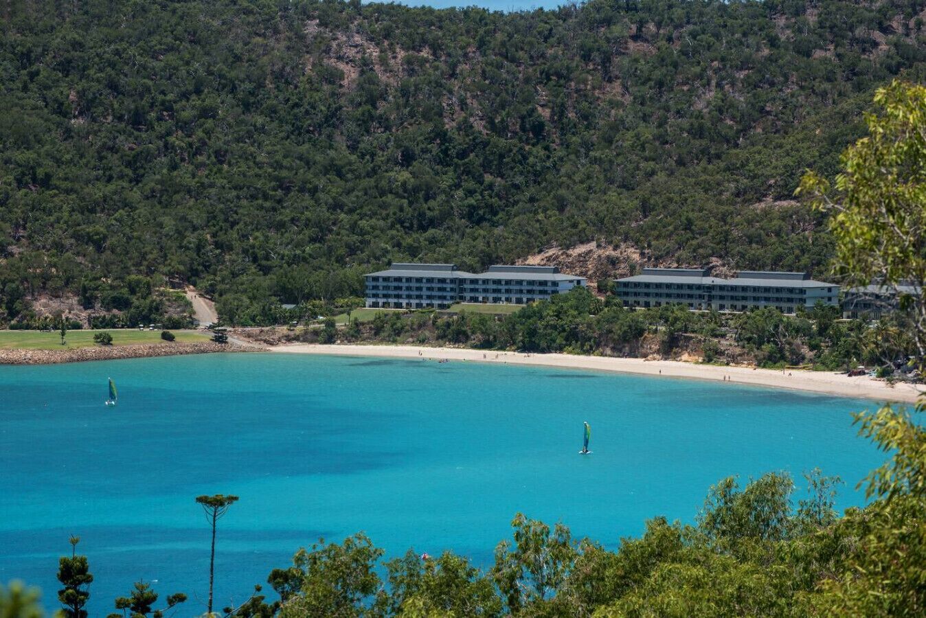 A coastal hotel with multiple buildings, a sandy beach, and clear blue waters.