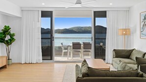 Un salon moderne doté d’une porte-fenêtre coulissante donnant sur un balcon avec vue sur un lac et des montagnes.