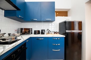 A modern kitchen with blue cabinets, a black refrigerator, and a microwave.