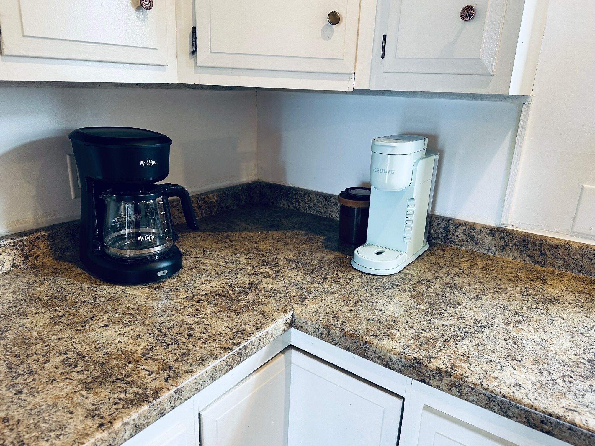 A kitchen with a granite countertop, a black coffee maker, and a white Keurig coffee maker.