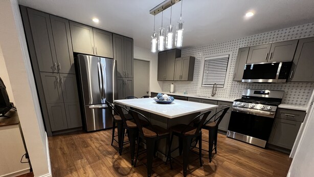 A modern kitchen with grey cabinets, a stainless steel refrigerator, a black stove, and a wooden dining table with four chairs. - Spacious 3 Bedroom Home in Ewing, NJ – Modern Comfort in a Prime Location (Trenton)