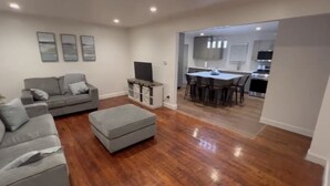 A modern living room with a grey sofa, ottoman, and a dining area with a table and chairs. - Spacious 3 Bedroom Home in Ewing, NJ – Modern Comfort in a Prime Location (Trenton)