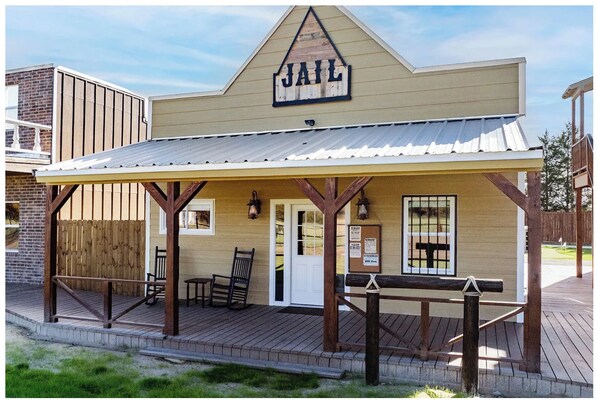 A jail building with a wooden porch, a sign reading 'JAIL,' and a brick wall in the background. - Texas Tombstone Vacation Rental (Eustace)