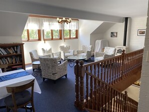 Relax in a spacious room with a high ceiling, featuring a wooden staircase, comfortable seating areas, and a quiet reading nook.