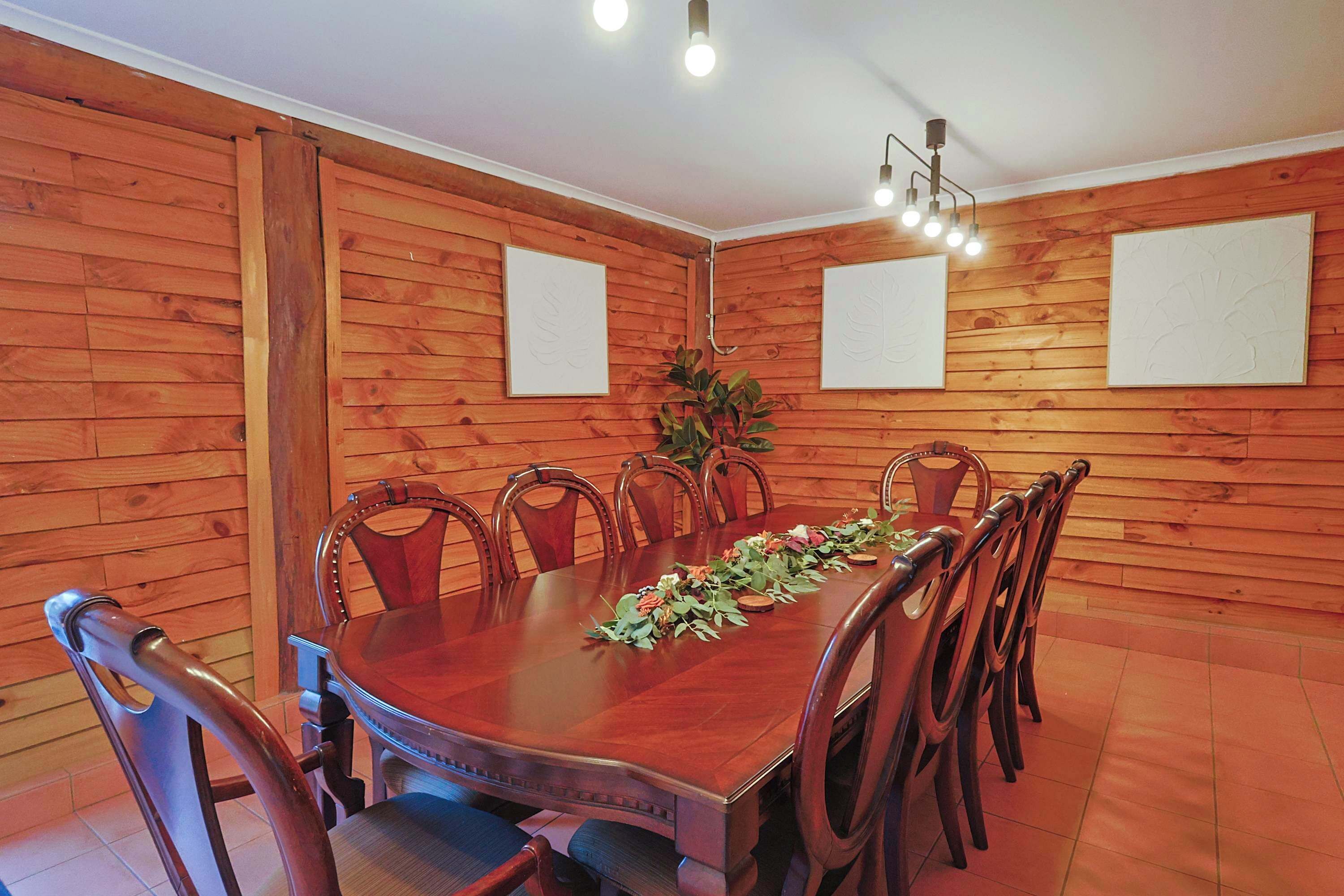 A wooden-paneled room with a round table and chairs, a potted plant, and wall-mounted light fixtures.