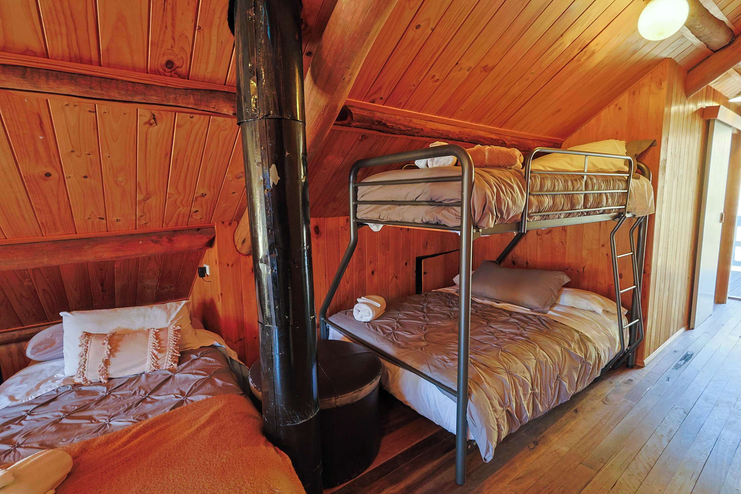 A wooden cabin room with bunk beds, a fireplace, and a window.
