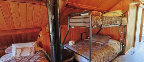 A wooden cabin room with bunk beds, a fireplace, and a window.