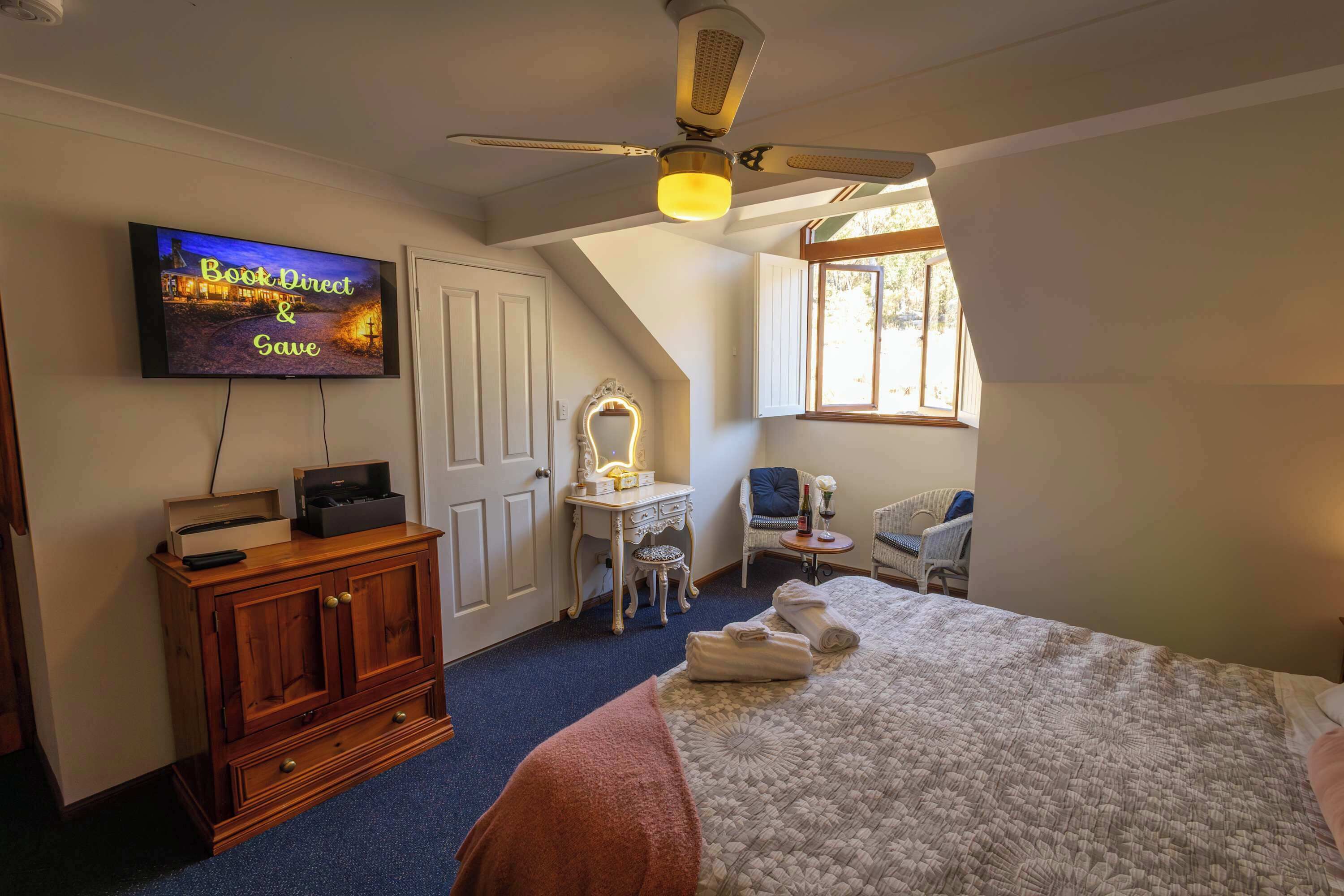 Une chambre à coucher comprenant un lit, un téléviseur fixé au mur, un ventilateur de plafond, une coiffeuse avec un miroir et une fenêtre.