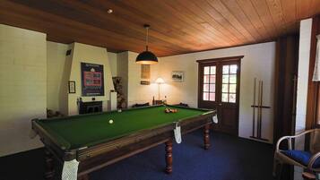 A pool table with a green felt surface, a hanging lamp, and a wooden ceiling.