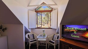 A cozy room with a TV, two wicker chairs, a small table, and a window with a view of trees.