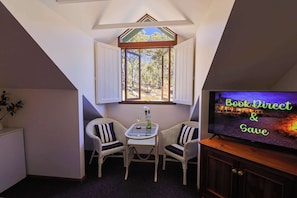 A cozy room with a TV, two wicker chairs, a small table, and a window with a view of trees. - Countryside Family Room (Eukey)