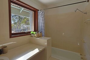 A bathroom with a bathtub, a shower, a window with a view, and a sink with plants.