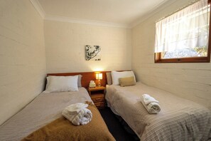 A twin room with two beds, a nightstand with a lamp, a wall art piece, and a window with curtains. - Countryside Family Room (Eukey)