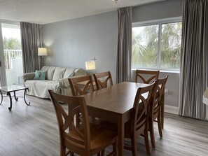 Uma sala de estar moderna com uma mesa de jantar e cadeiras, um sofá, um abajur e grandes janelas com cortinas.
