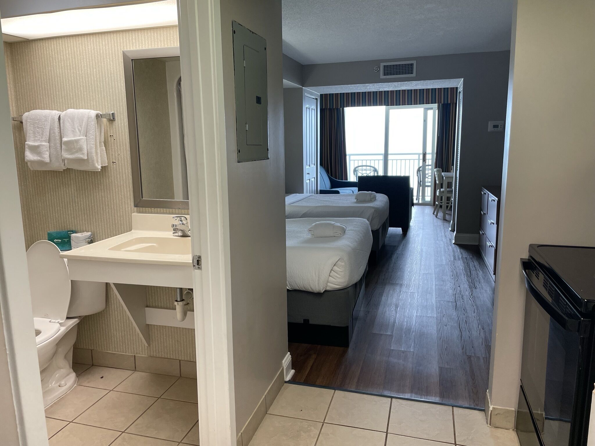 Et hotelværelse med badeværelse, håndvask, toilet, to senge og balkonudsigt.