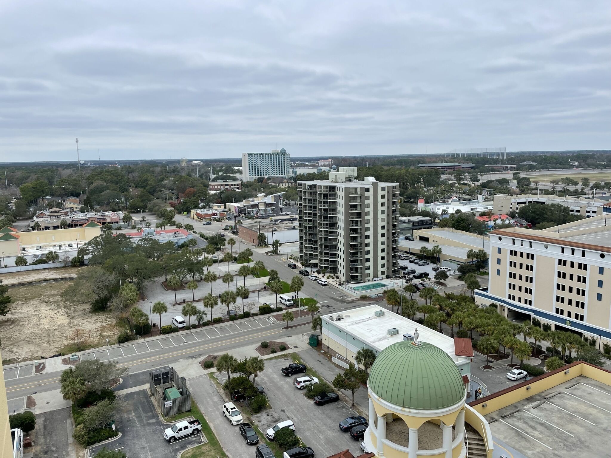 A high-rise building with multiple floors, a parking lot, and a green-roofed structure.
