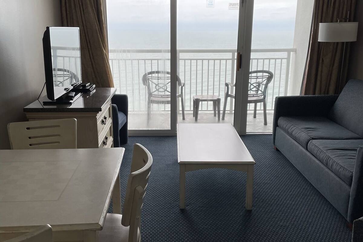 Une chambre d’hôtel avec un balcon, un coin repas comprenant une table et des chaises, un canapé et un bureau avec un ordinateur.