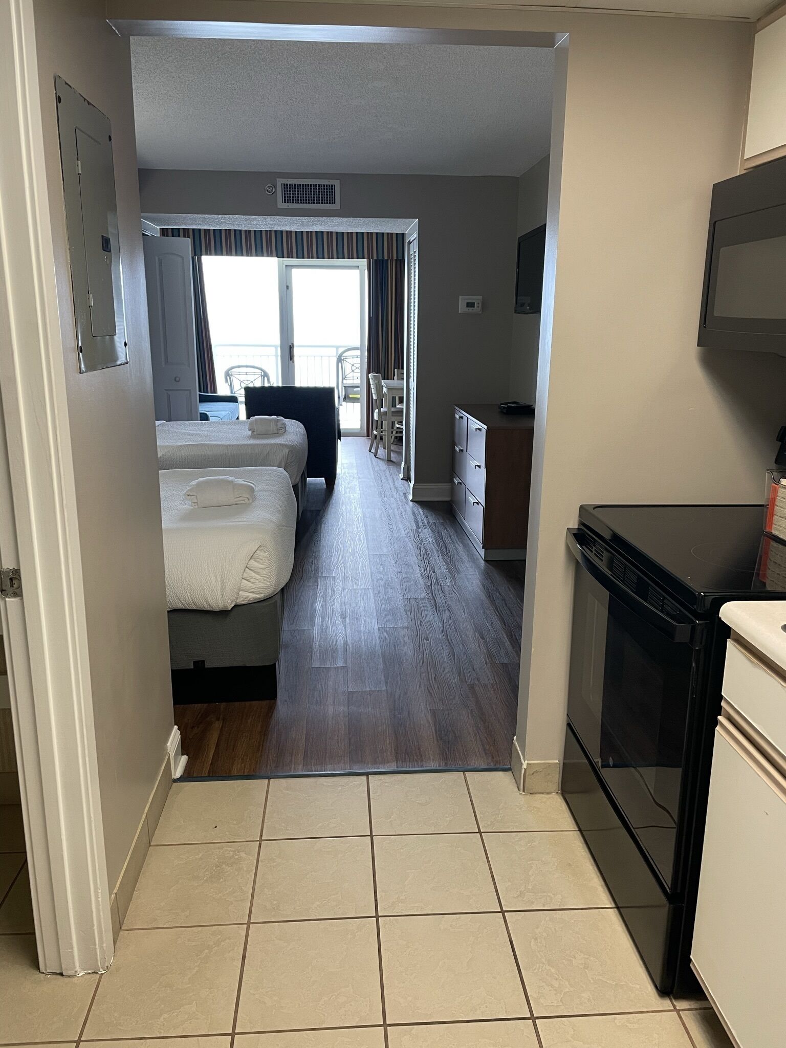 A hotel room with two beds, a kitchenette, a dining area, and a view of the outdoors.
