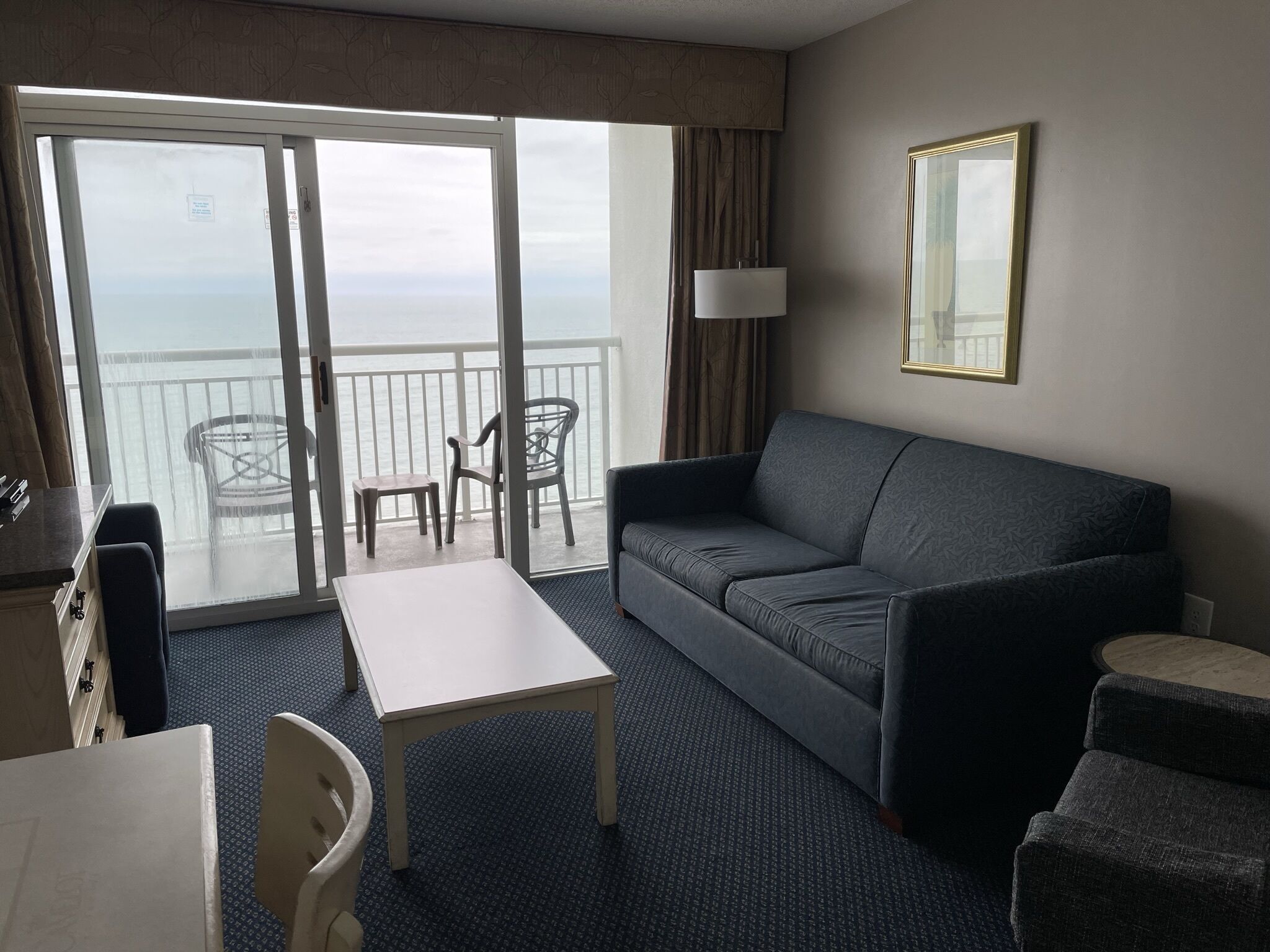A hotel room with a balcony, a sofa, a table, and a chair.