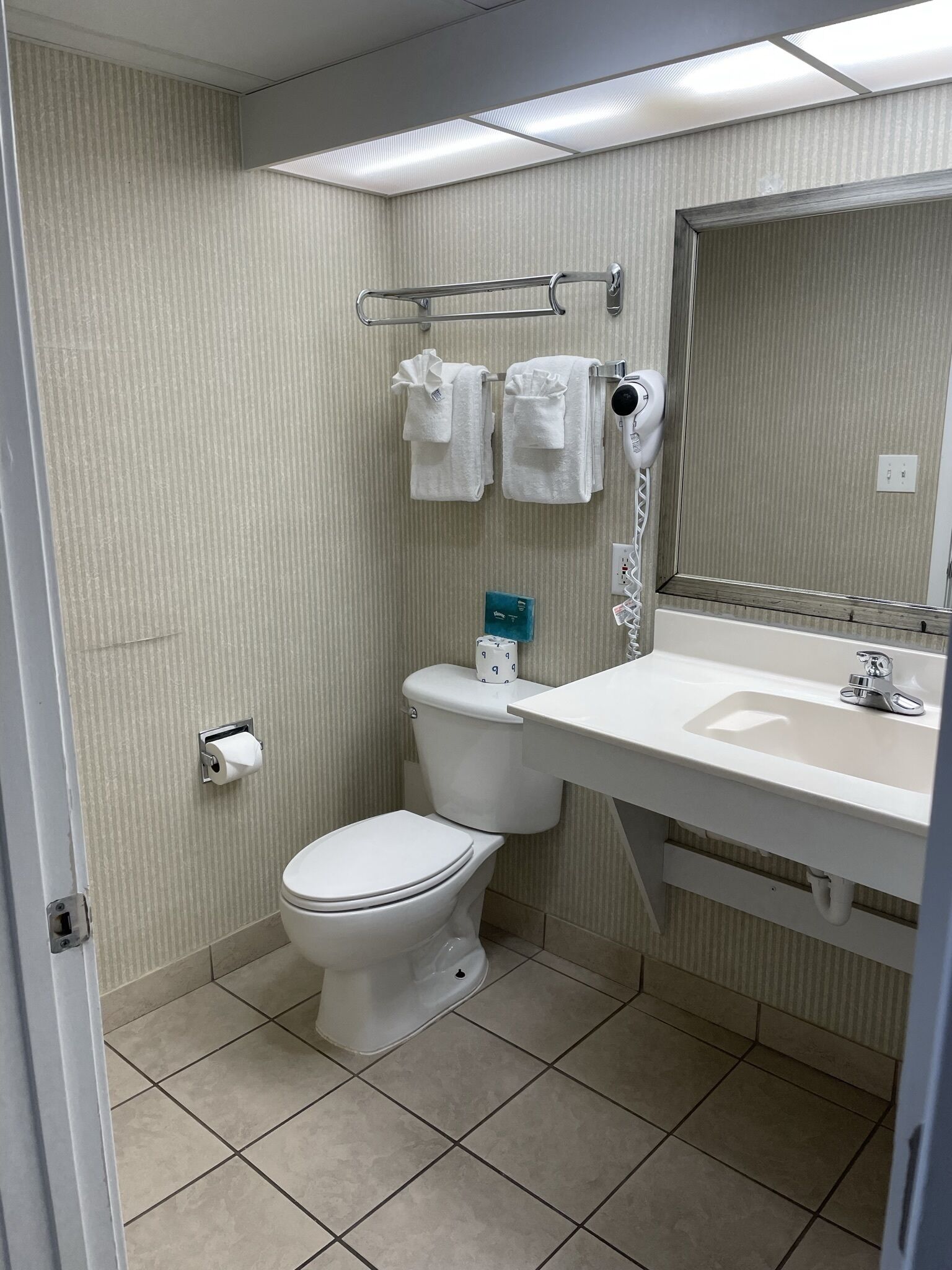A bathroom with a toilet, a sink, a towel rack with two towels, a paper towel dispenser, and a mirror.