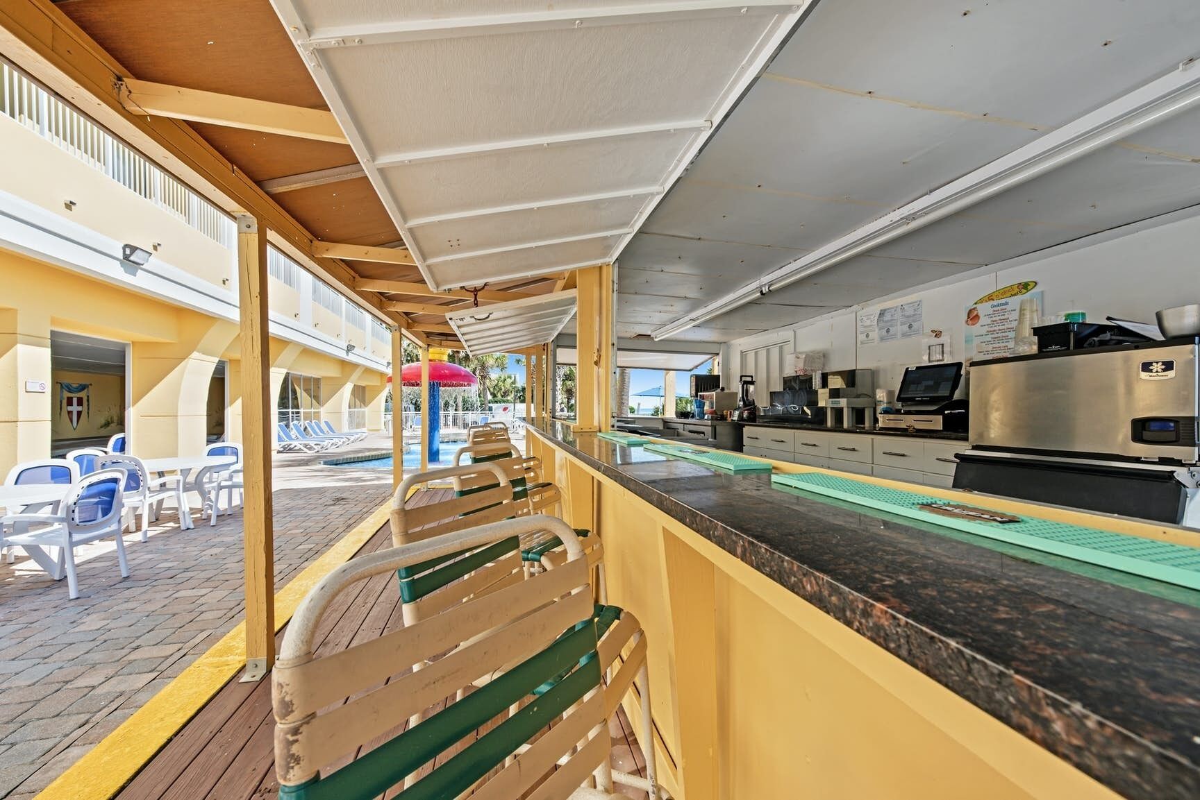 A restaurant with outdoor seating, a counter, and a view of the pool area.