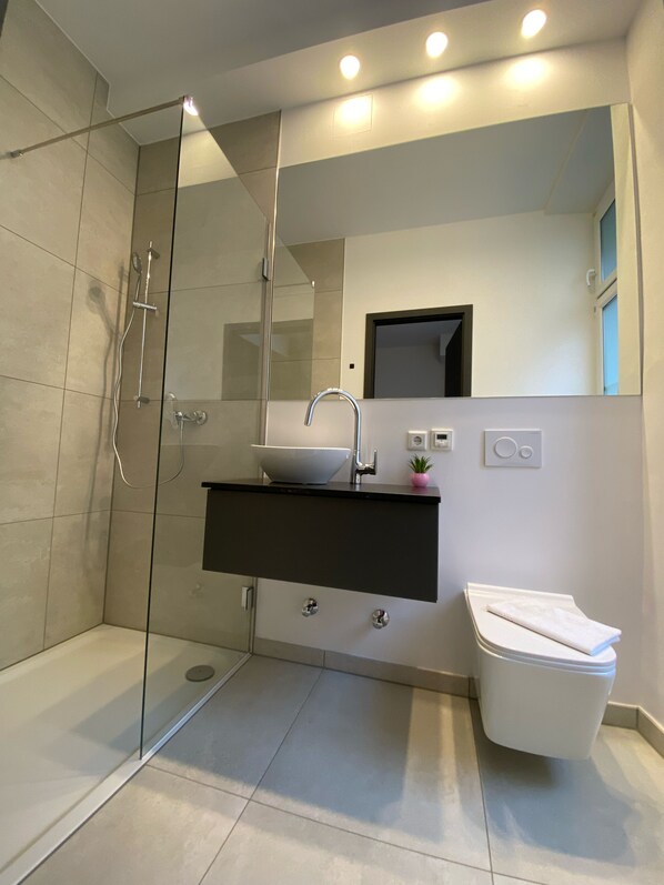 A modern bathroom with a glass-enclosed shower, a white sink with a black countertop, and a white toilet.