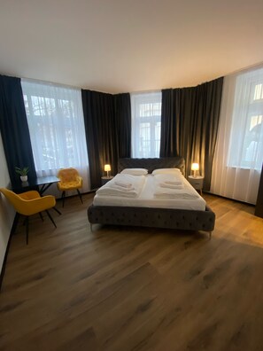 A bedroom with a large bed, two bedside lamps, a yellow chair, and a small table.