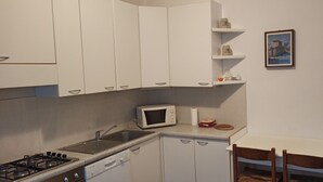 Una piccola cucina con mobili bianchi, un forno a microonde, un lavello, un piano cottura e un tavolo da pranzo con sedie.