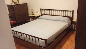 Un letto singolo con struttura e testiera in legno, un comodino con lampada e una cassettiera.