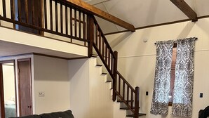 A spacious living room with a wooden staircase, a grey sofa, a patterned throw, and a stone accent rug. - Cabin joins Lost River State Park! Convenient to most popular hiking trail.  (Mathias)