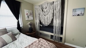 A bedroom with a bed, a bedside table, a mirror, and macramé curtains.