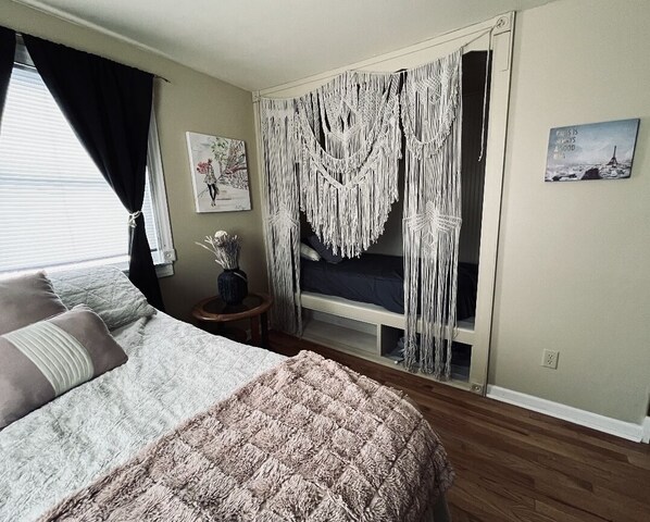 A bedroom with a bed, a bedside table, a mirror, and macramé curtains.