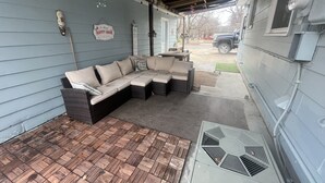 A covered patio area with a sectional sofa, a small table, and a decorative sign.