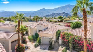 A residential area with houses featuring red-tiled roofs, surrounded by palm trees and flowering plants, with mountains in the background. - La Quinta Resort-Style Retreat (La Quinta)