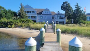 A wooden boardwalk leading to a large house with multiple stories and a balcony.