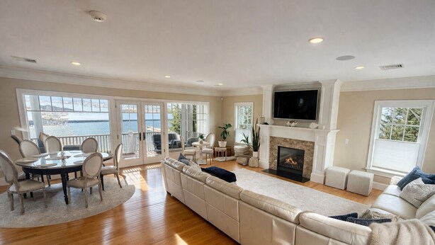 A spacious living room with a large sofa, a dining table with chairs, a fireplace, and a TV mounted on the wall.