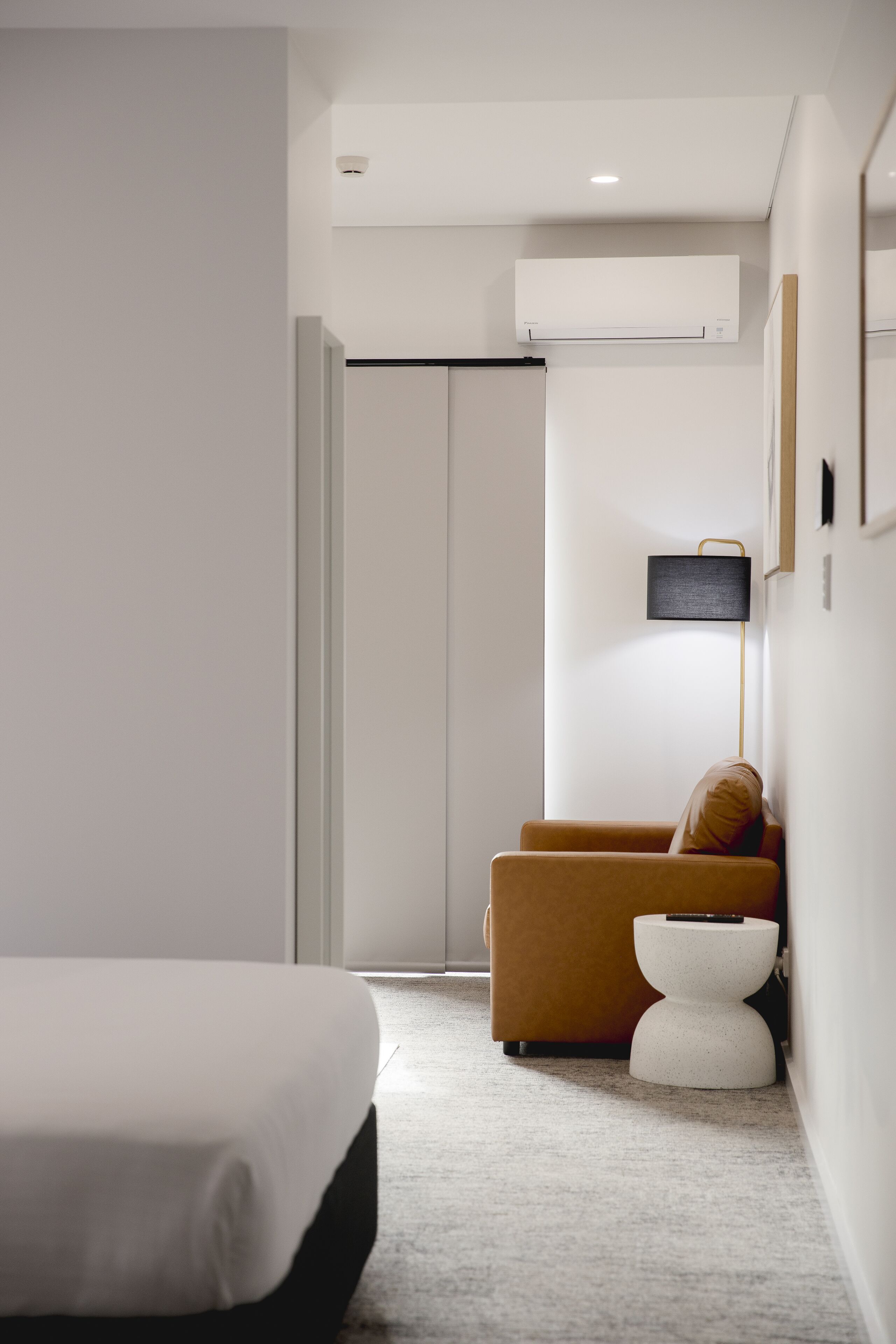 Ein modernes Hotelzimmer mit einem Bett, einer Couch, einem kleinen weißen Hocker und einer wandmontierten Klimaanlage.