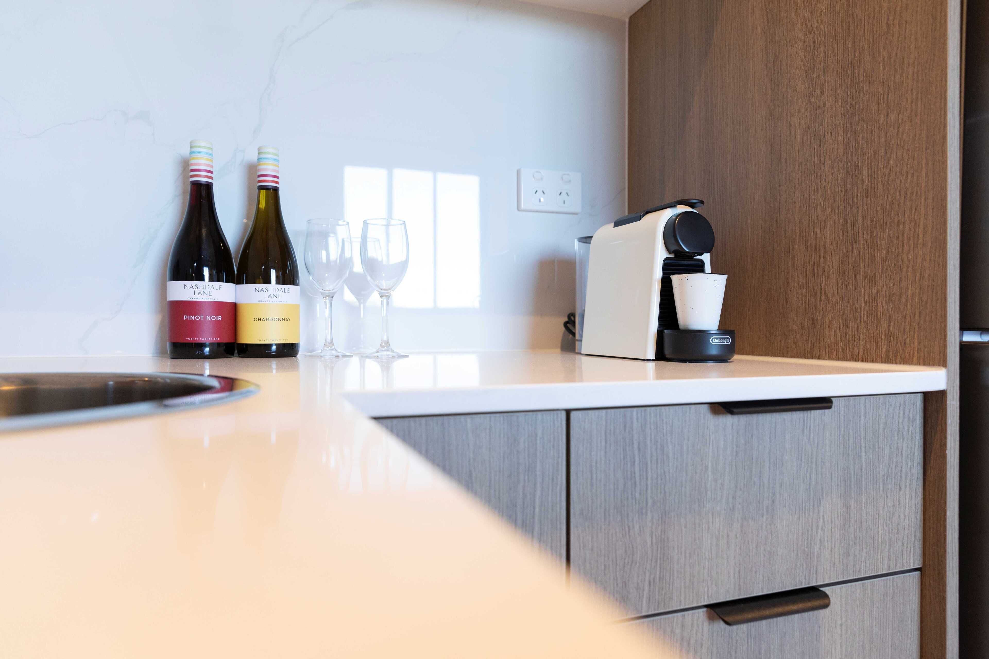 A kitchen counter with two wine bottles, a coffee maker, and three wine glasses.