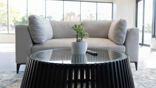 A modern room with a round glass coffee table, a beige sofa, and a potted plant. - Amica Serviced Apartments (Orange)