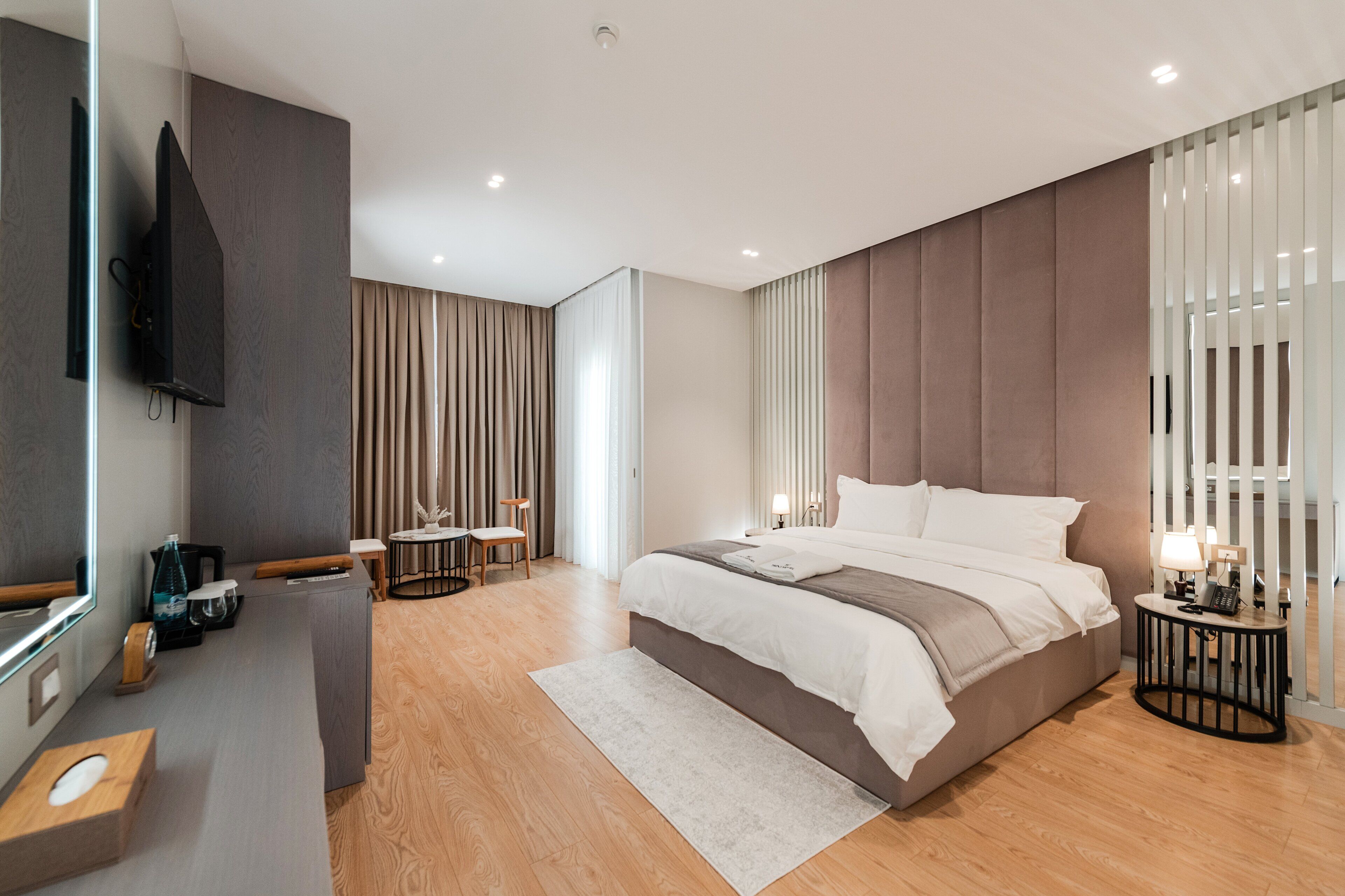 Una habitación de hotel moderna con una cama grande, un escritorio con una silla, un televisor de pantalla plana y un amplio ventanal con persianas.