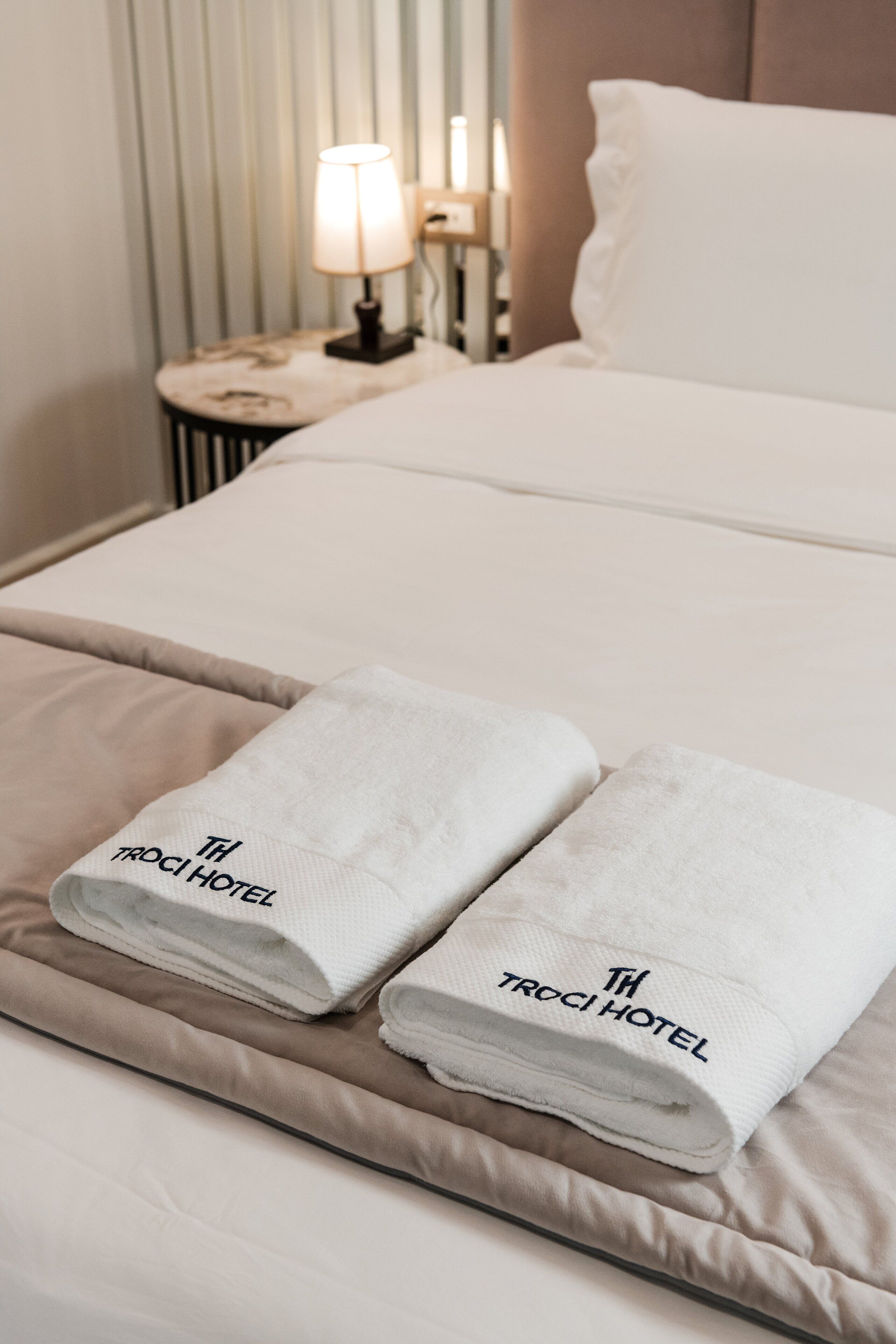 A neatly made bed with two folded towels on a beige bedspread.
